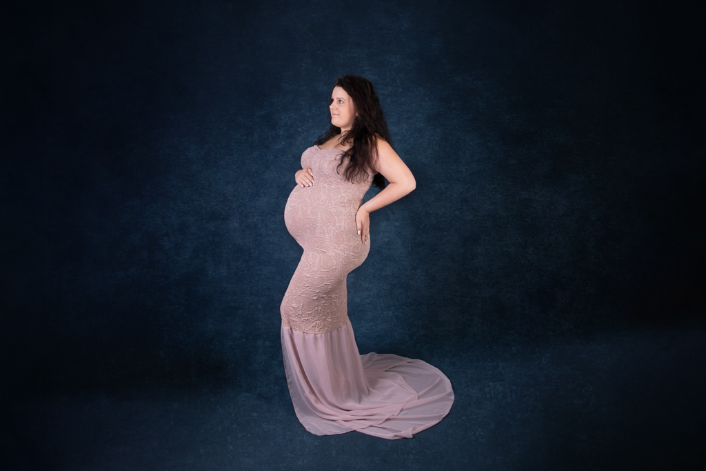 Schwangere im altrosafarbenen Kleid vor dunklem Hintergrund