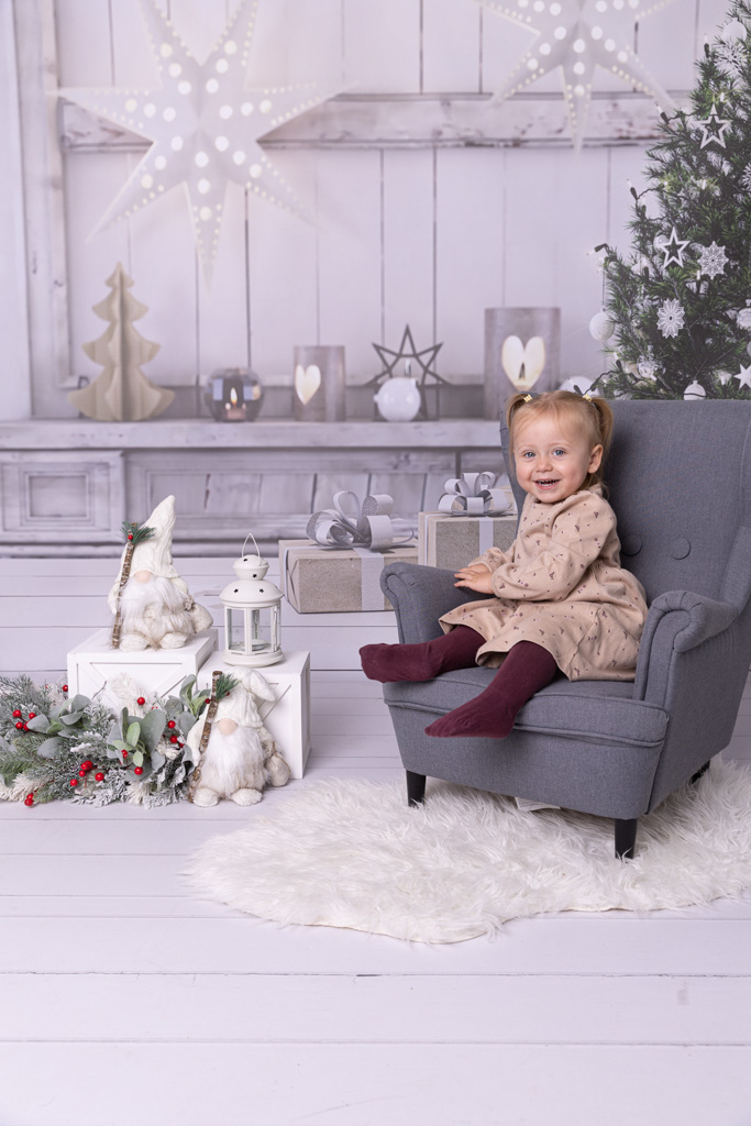 Mädchen sitzt auf einem grauen Sessel, hinter sieht man ein weihnachtliches Set Up