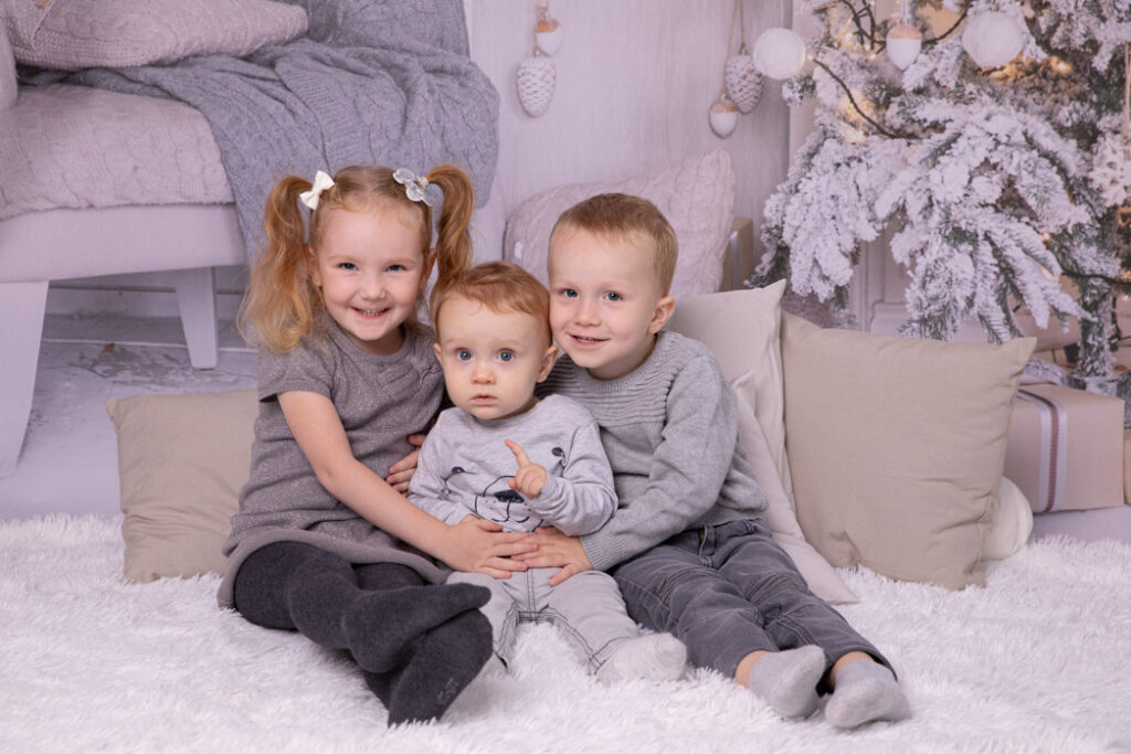 Drei Kinder sitzen zusammengekuschelt auf einer Decke und lehnen sich an Kissen an. Weihnachten