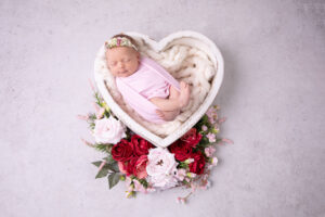 schlafendes Baby liegt in einer Herzschale, ist gepuckt und sie ist umgeben von Rosen