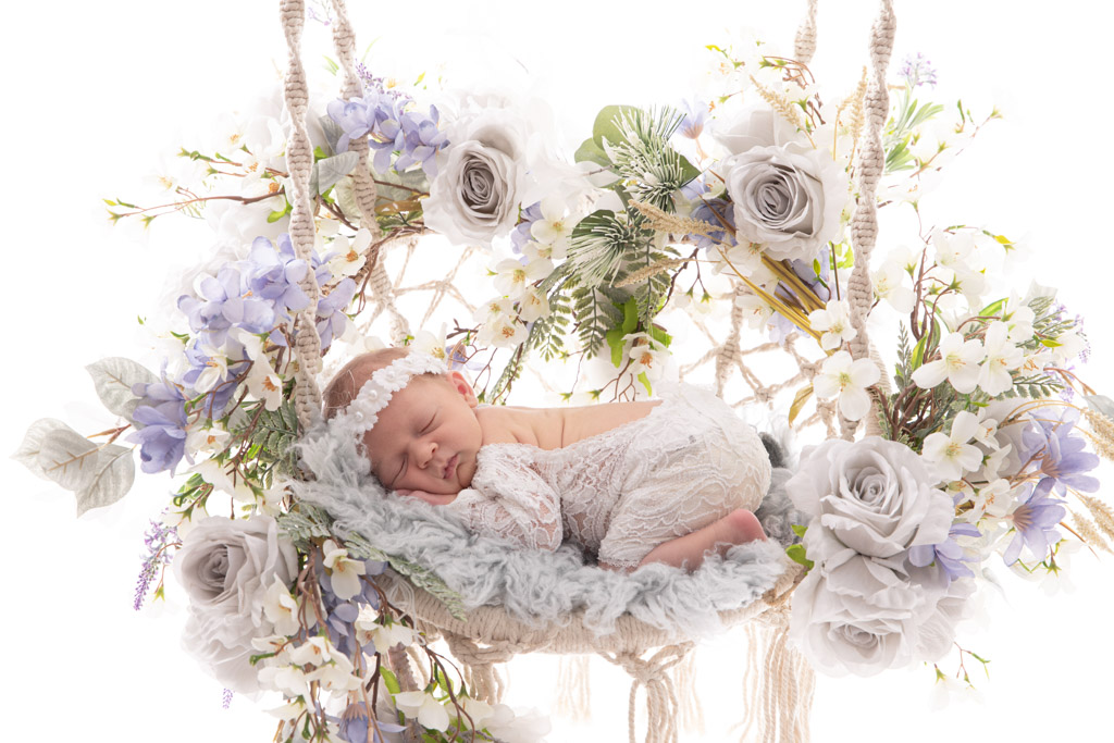 Baby liegt in einer Schaukel umgeben von einer schönen Blumengirlande