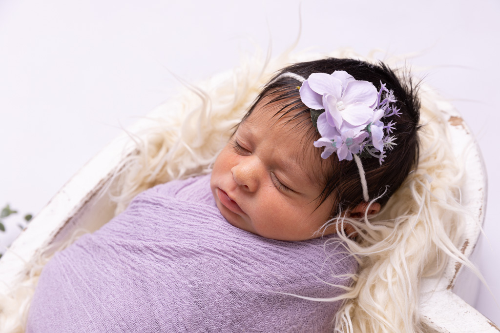 Baby liegt eingewickelt in einer lilafarbenen Decke und trägt ein Haarband