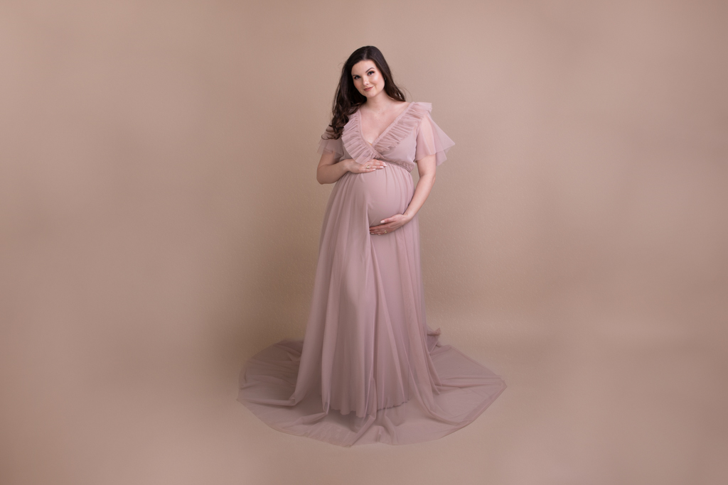 Schwangere im hautfarbenem Kleid vor beigem Hintergrund in Lohmar von Fotografie Carina Rosen