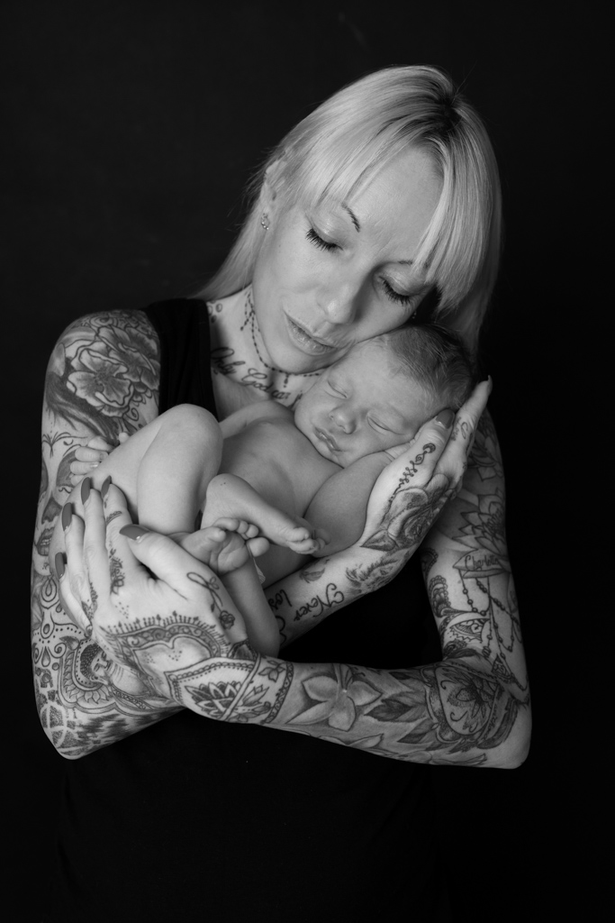 Mama mit vielen Tattoos hält ihr schlafendes Neugeborene im Arm von Fotografie Carina Rosen bei köln